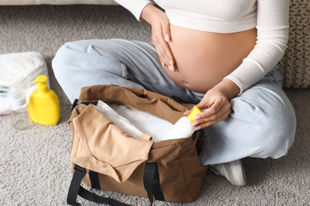 Young pregnant woman packing baby bottle into maternity hospital bag at homeの写真素材