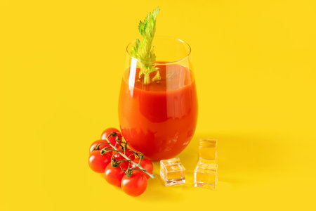 Glass of bloody mary with celery, tomatoes and ice cubes on yellow backgroundの写真素材