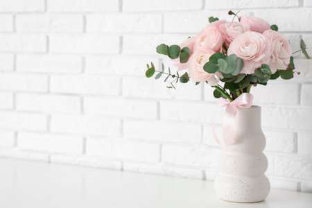 Vase with bouquet of beautiful ranunculus flowers on table near white brick wall, closeupの写真素材