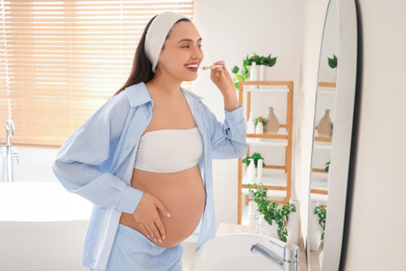 Young pregnant woman brushing teeth near mirror in bathroomの写真素材