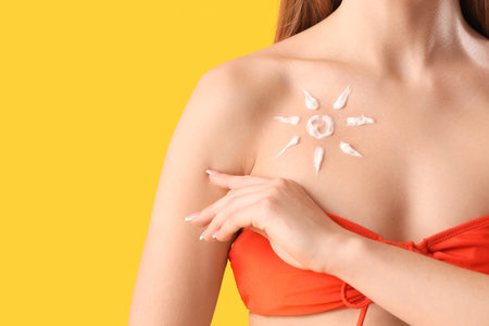 Young woman in swimsuit with sun made of sunscreen cream on yellow background, closeup