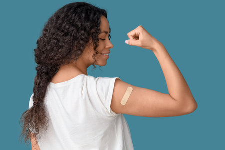 Young African-American woman with medical patch showing muscles after vaccination on blue background, back viewの写真素材