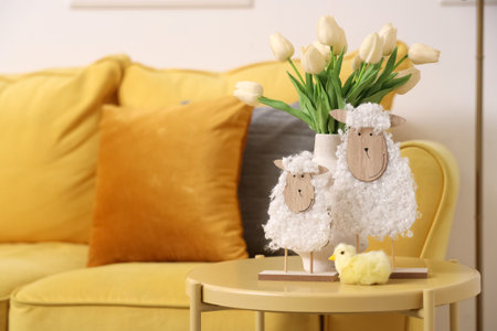 Cute sheep with Easter baby chicken and tulip flowers on coffee table near yellow sofa in festive living roomの写真素材