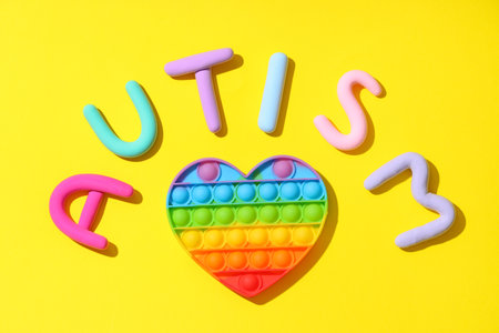 Pop it fidget toy and word AUTISM made from plasticine on yellow backgroundの写真素材