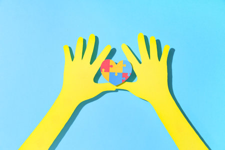 Paper hands holding colorful puzzle pieces in shape of heart on blue background. Autistic disorder conceptの写真素材