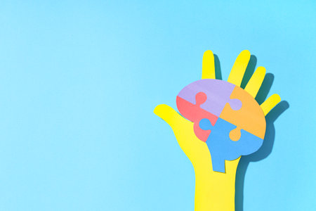 Paper hand holding colorful puzzle pieces in shape of brain on blue background. Autistic disorder conceptの写真素材
