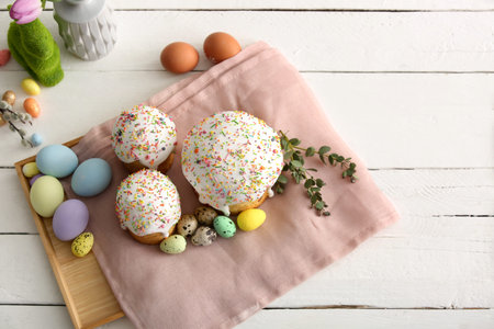 Sweet Easter cakes with painted eggs and eucalyptus branches on white wooden background