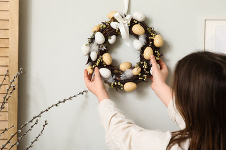 Young woman hanging Easter wreath on light wall at home, closeupの写真素材