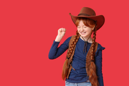Cute happy teenage girl in cowboy hat on red backgroundの写真素材