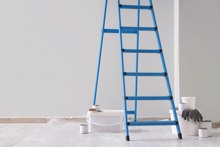 Blue stepladder with paint cans near light wall in roomの写真素材
