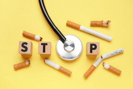 Cubes with the word STOP, stethoscope and cigarette butts on yellow background. No Tobacco Day