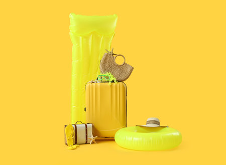 Suitcases with inflatable mattress, ring, summer bag and beach accessories on yellow background. Vacation conceptの写真素材