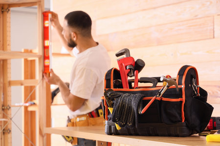 Male construction worker working with level and bag of tools in office