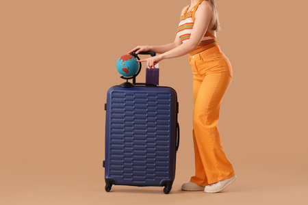 Young woman with suitcase and passport pointing at globe on beige background, closeup. Travel conceptの写真素材