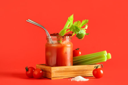 Mason jar of bloody mary cocktail with bacon and celery on red backgroundの写真素材