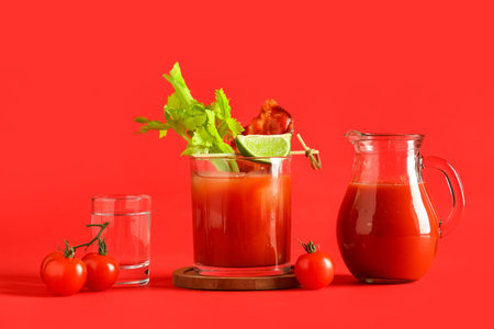 Glass of bloody mary cocktail with bacon and ingredients on red backgroundの写真素材