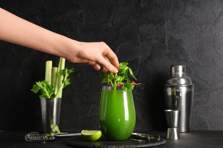 Female hand with celery and glass of green bloody mary cocktail with bacon on black backgroundの写真素材