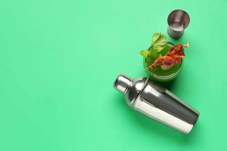 Glass of green bloody mary cocktail with bacon and shaker on color backgroundの写真素材