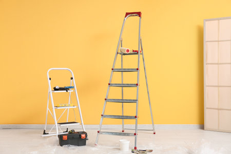 Maintenance ladders with instruments and paint tools near yellow wallの写真素材