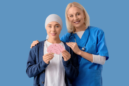 Young woman after chemotherapy with paper brain and nurse on blue background