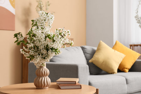Vase of white blooming branches with books on coffee table near sofa in living room, closeupの写真素材
