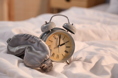 Alarm clock with sleeping mask on bed at night, closeupの写真素材