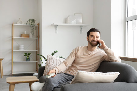 Young man talking by mobile phone on sofa near air conditioner at homeの写真素材