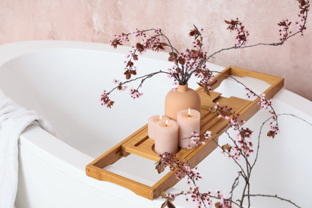 Vase with blossoming branches and burning candles on stand in bathroom, closeup