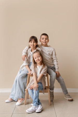 Cute little friends sitting on stool near beige wallの写真素材