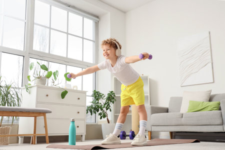 Sporty little boy in headphones exercising with dumbbells at homeの写真素材