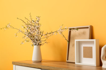 Dresser with vase of white blooming branches and decor near yellow wall in living roomの写真素材