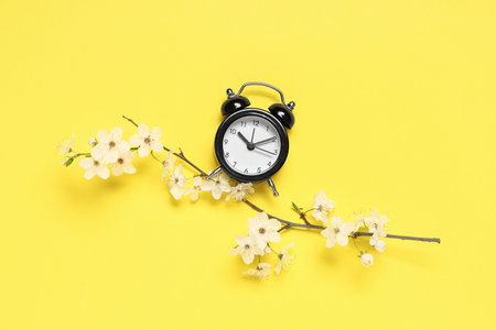 Alarm clock and blooming branch on yellow background. Spring time