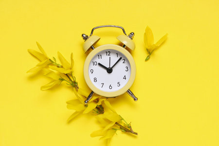 Alarm clock and blooming branch on yellow background. Spring time