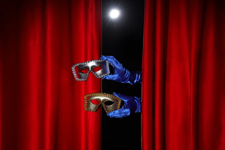 Female hands in gloves with carnival masks behind red curtains on dark background