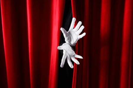 Female hands in white gloves behind red curtains on dark backgroundの写真素材