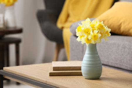 Vase with narcissus flowers and books on coffee table against sofa in living room, closeupの写真素材