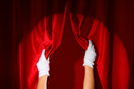 Female hands in white gloves opening red curtains on color backgroundの写真素材