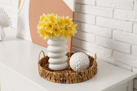 Vase with narcissus flowers and decor on dresser near white brick wall in living room, closeup