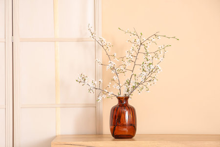Folding screen and blooming tree branches on dresser near beige wall
