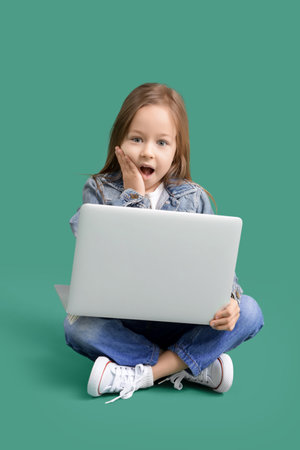 Surprised little girl with laptop sitting on green backgroundの写真素材
