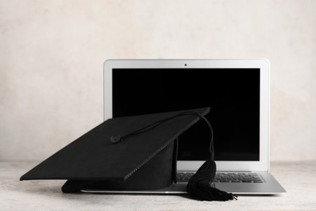 Mortar board and modern laptop on white backgroundの写真素材