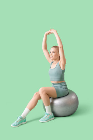 Sporty blonde woman stretching on fitball against green backgroundの写真素材