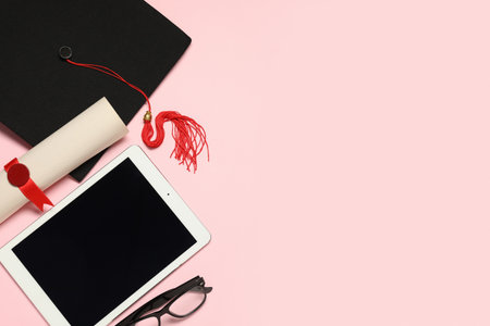 Mortar board with diploma, eyeglasses and modern tablet computer on pink backgroundの写真素材