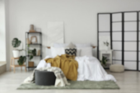 Blurred view of light bedroom with folding screen, bookshelf and tableの写真素材