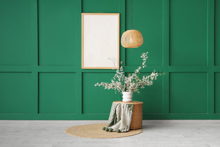 Vase of blooming branches on wicker table and hanging frame near green wall in living roomの写真素材