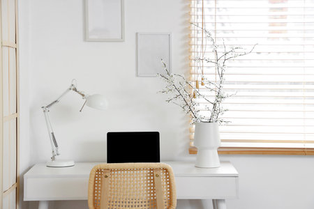 Vase of blooming branches with laptop and lamp on table in living roomの写真素材
