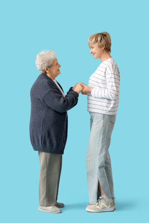 Mature woman with her mother holding hands on blue backgroundの写真素材