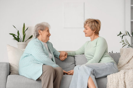 Senior woman with her daughter holding hands on sofa at home. Mother's Day celebration