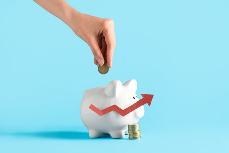 Female hand with piggy bank, coins and arrow on blue background. Concept of rising priceの写真素材