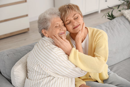 Mature woman with her mother hugging on sofa at homeの写真素材